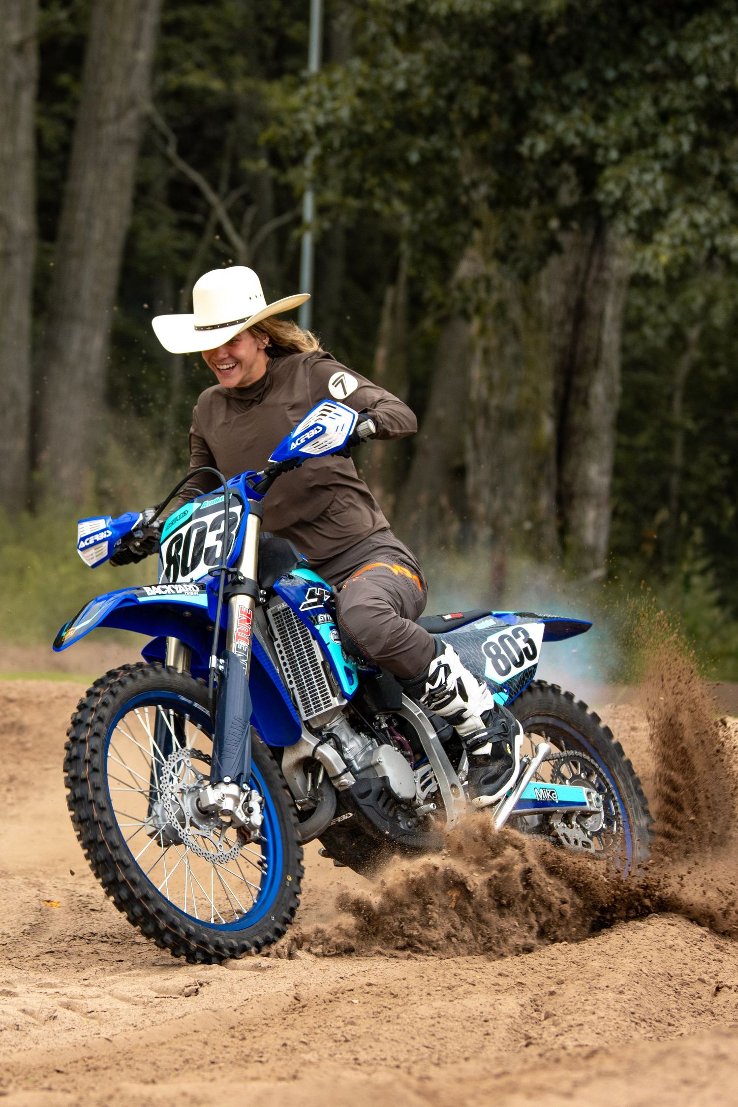 Dirt bike rider performing dynamic turns and slides through dusty terrain on a blue motorcycle.
