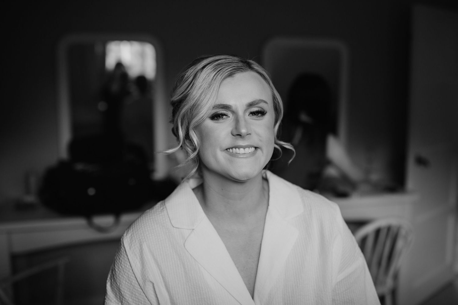 Black and white wedding portrait of a bride smiling in a white robe during wedding preparations.