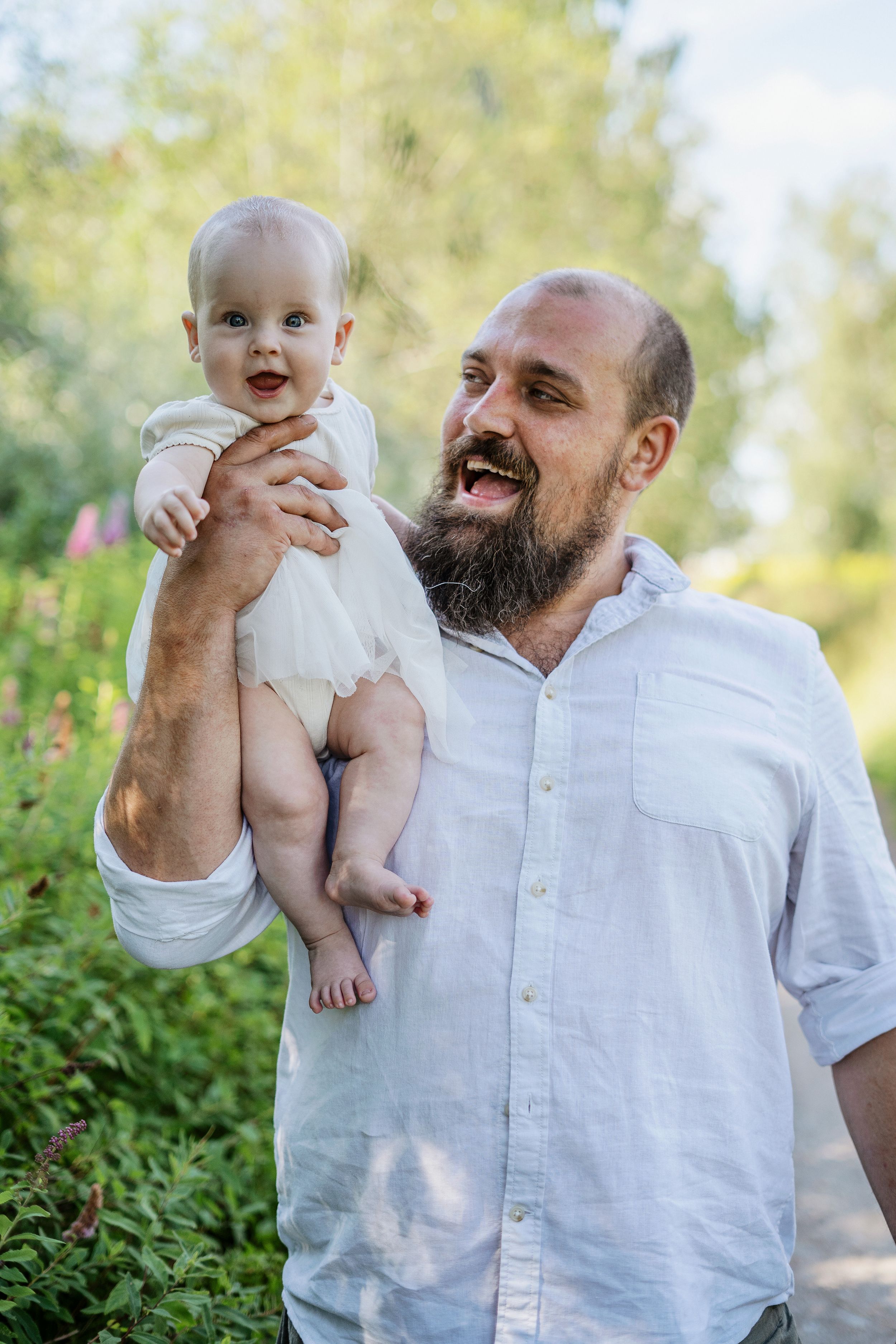 Pappa håller sitt lilla barn i famnen under en familjefotografering utomhus. En varm och lekfull stund i den gröna naturen.