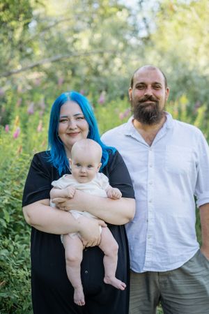 Familjefotografering utomhus med föräldrar och deras lilla barn i en grön och lummig miljö.