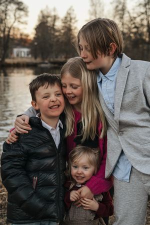 A family shares warm embraces and laughter together during an outdoor photo session by a lake at sunset. - Fotograf Emma Matkoski