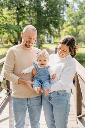 A joyful candid sequence of a family laughing and playing together on a wooden bridge in a sunny outdoor setting. - Fotograf Emma Matkoski