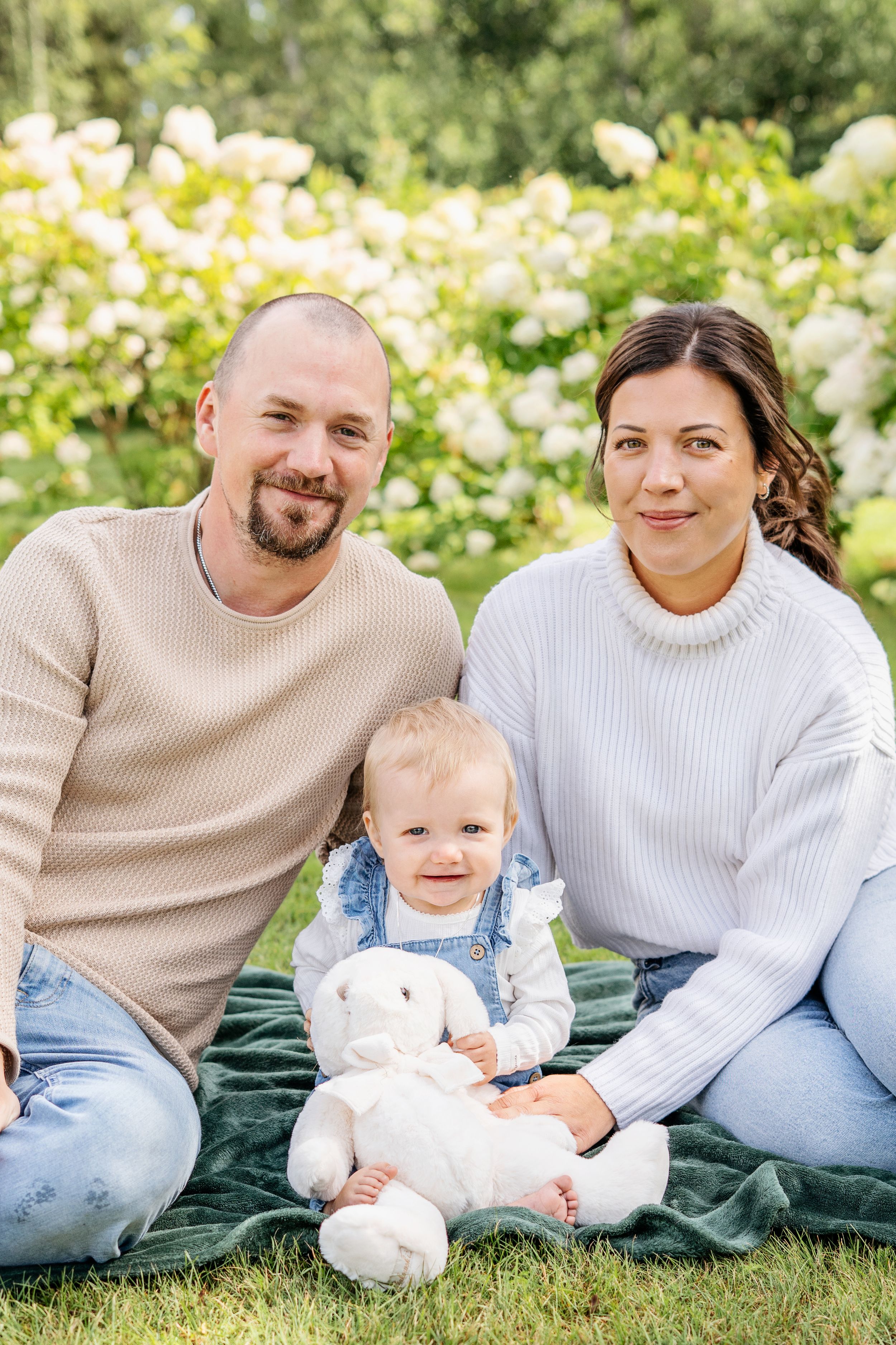 Familjen slappar tillsammans på en grön filt utomhus omgiven av vita blommor på en solig dag. - Fotograf Emma Matkoski