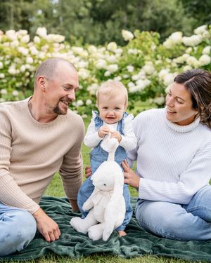 Familjen slappar tillsammans på en grön filt utomhus omgiven av vita blommor på en solig dag. - Fotograf Emma Matkoski