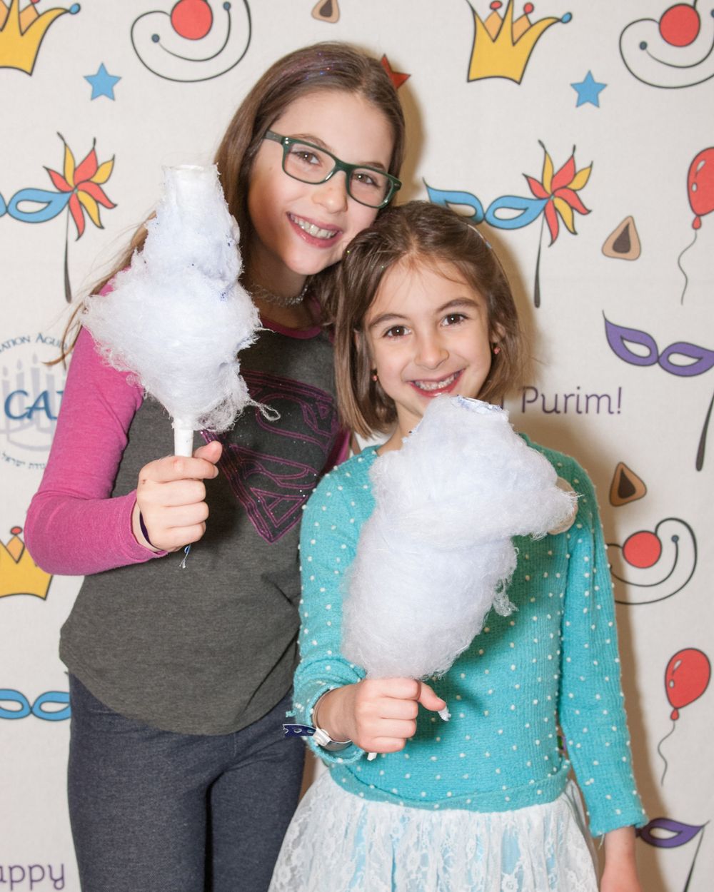 Party goers holding cotton candy at a Purim celebration with festive backdrop.