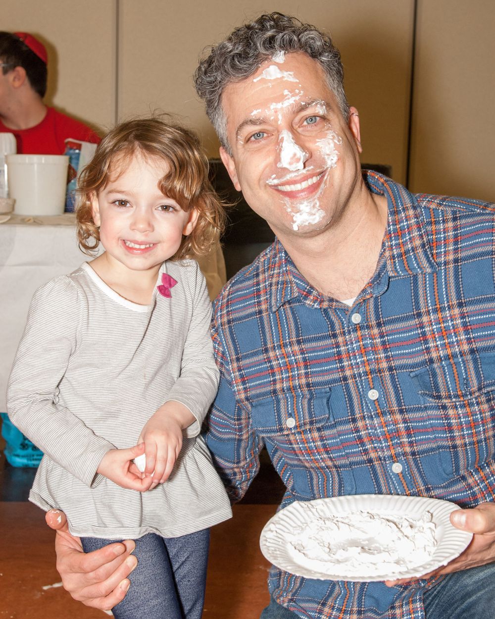 Two people pose together while holding a decorative plate indoors.