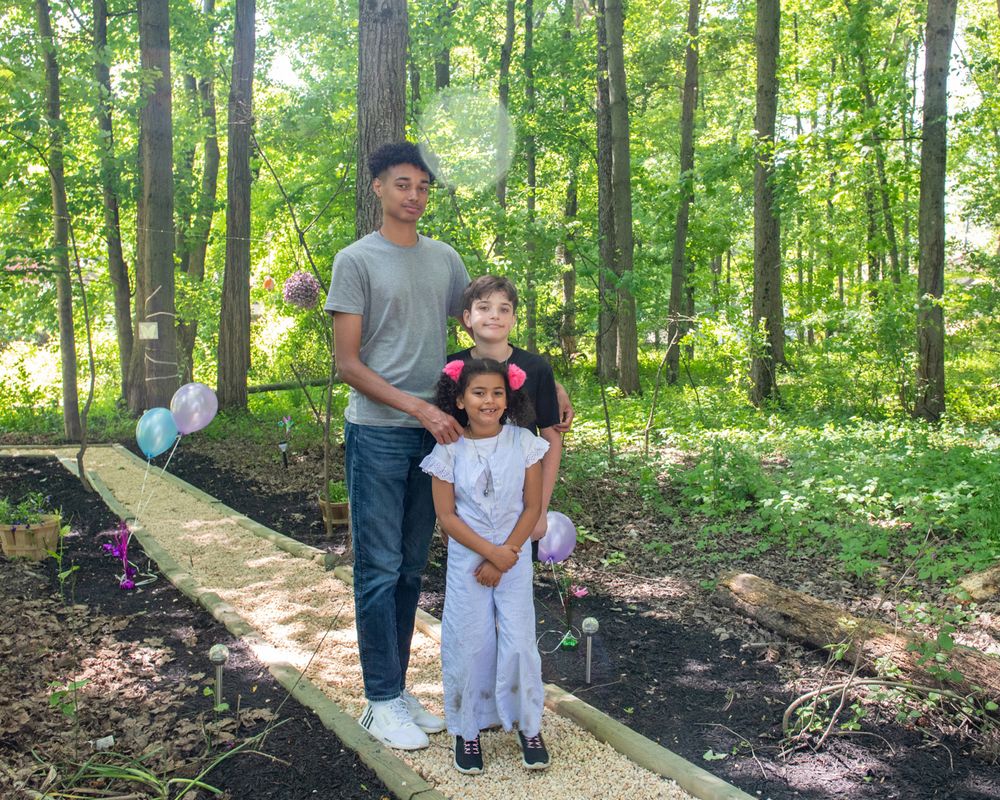 People stand together on a garden pathway surrounded by lush greenery and flowers.