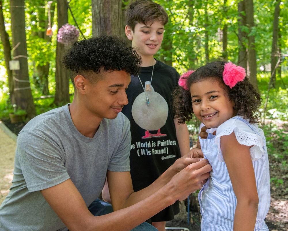 People share a moment looking at something together in a green forest setting.
