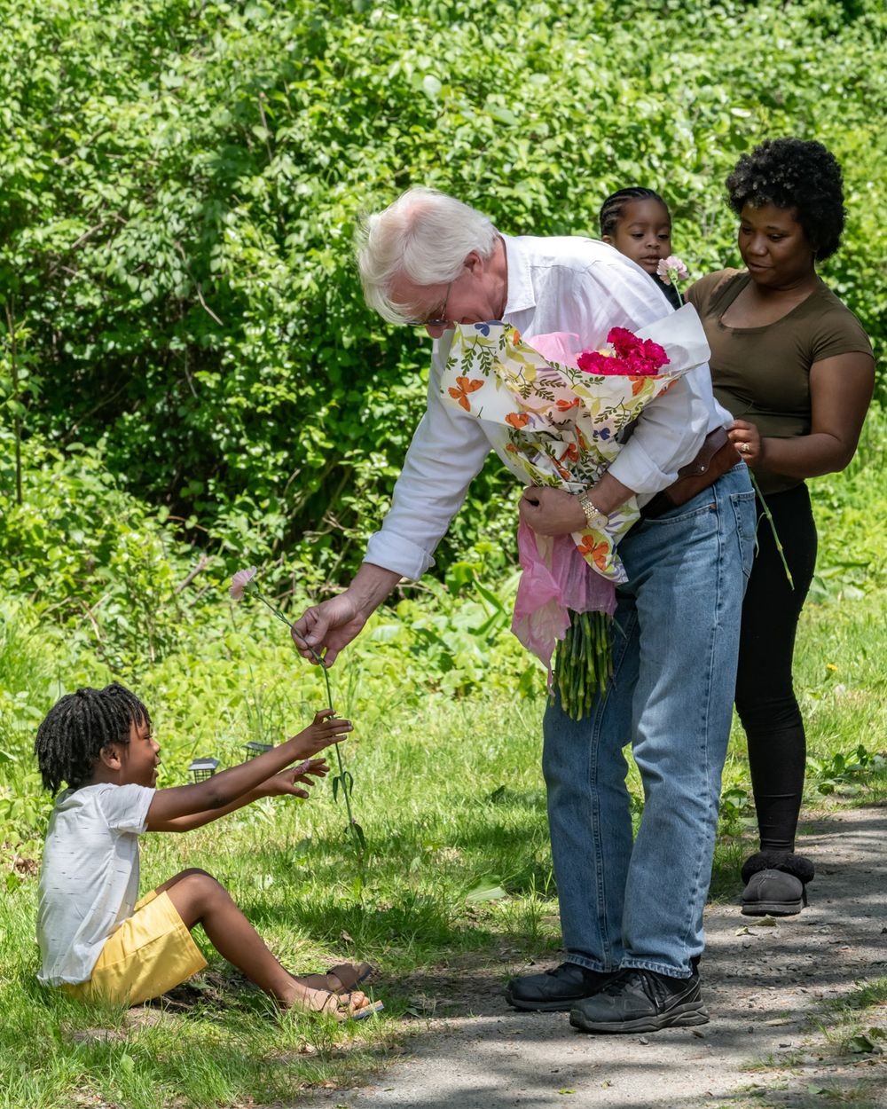 People sharing flowers on a garden path surrounded by lush greenery.