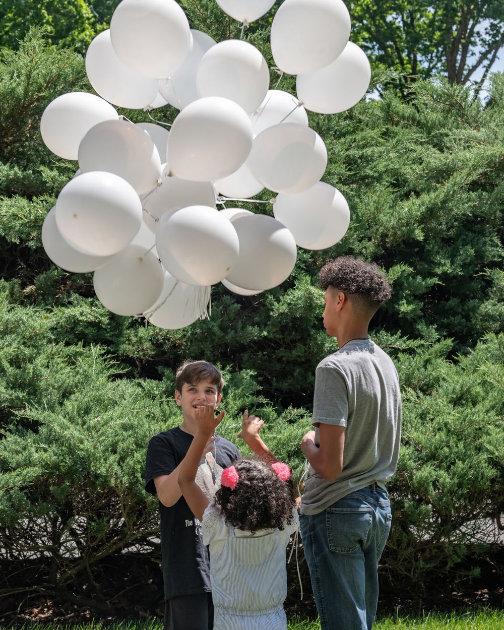 People stand with white balloons in a garden setting on a sunny day.