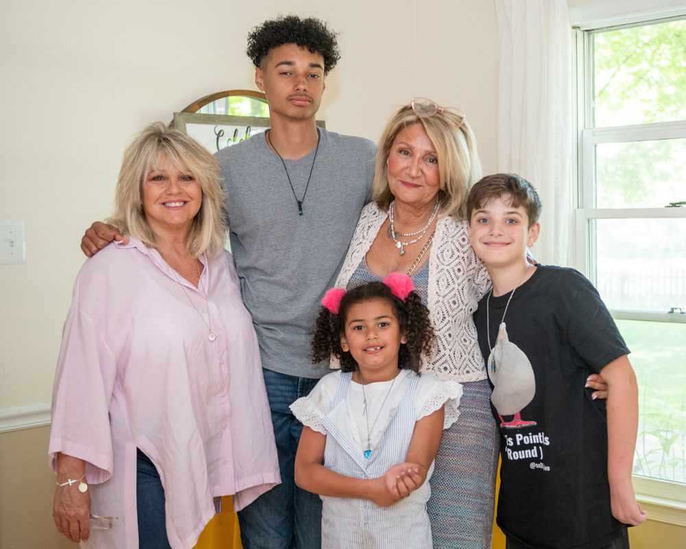 Multi-generational family group poses together in bright home interior.