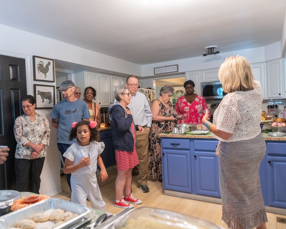 Group of people gathered in kitchen with blue cabinets during social gathering.
