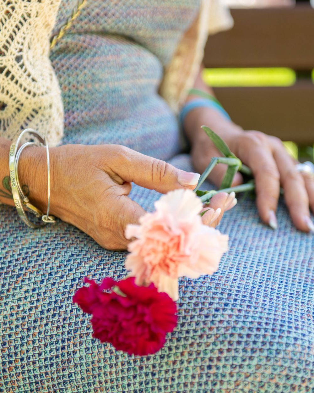 Close-up of hands holding pink and red carnations against blue fabric.