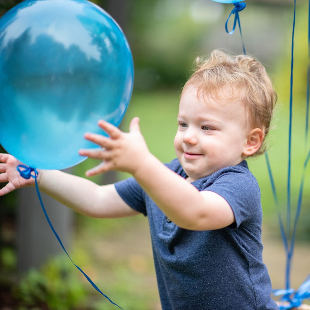 A toddler in a navy shirt playing with bright blue balloons outdoors.