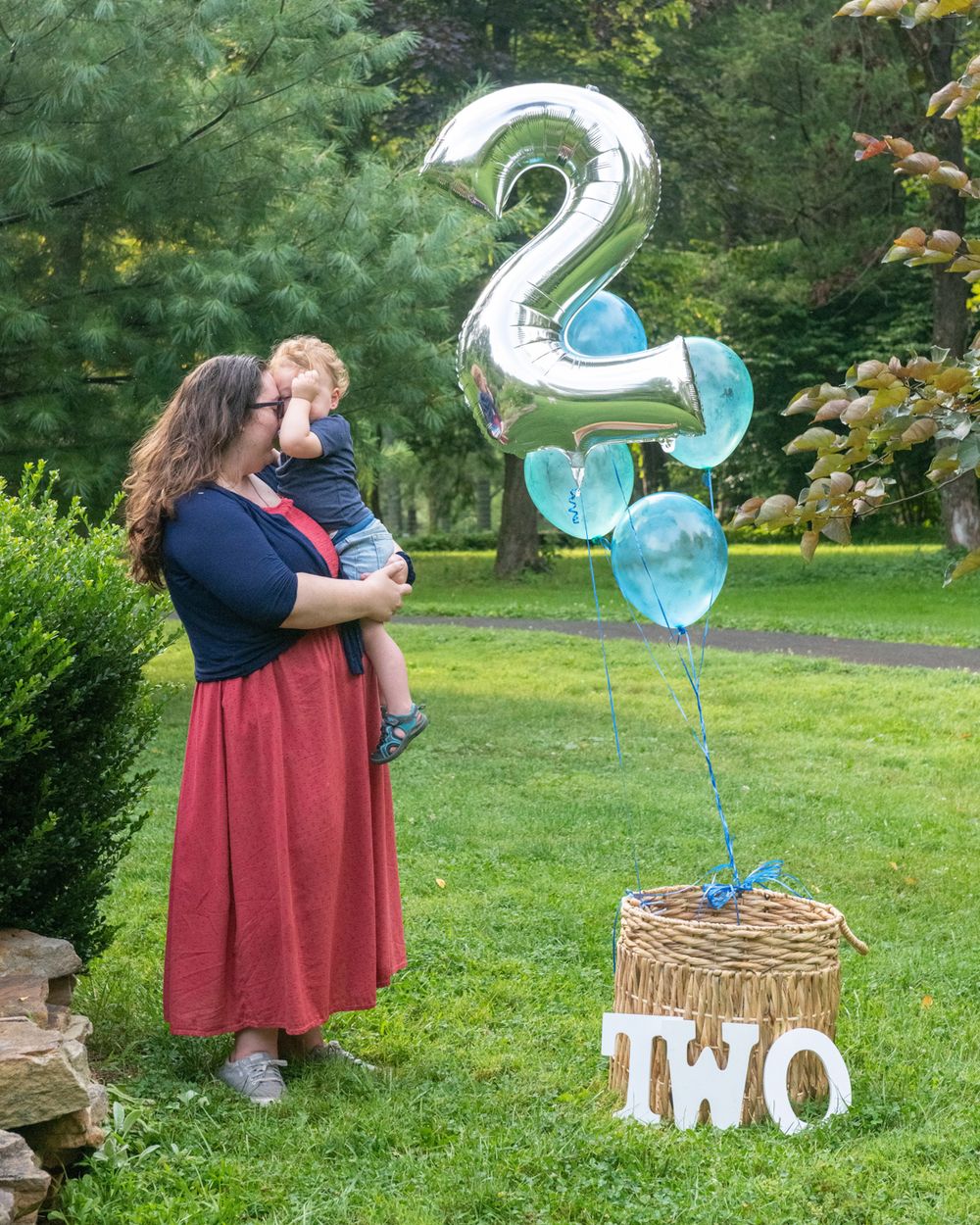 A second birthday celebration with a large silver number 2 balloon and blue decorations in an outdoor garden setting.