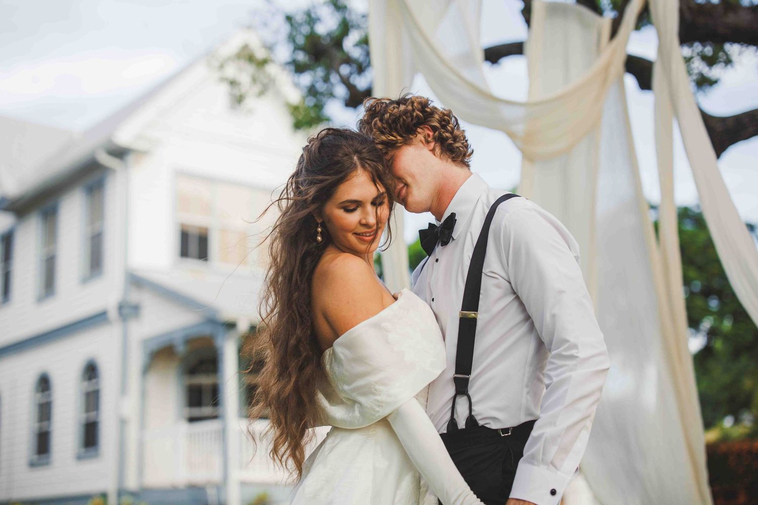 Intimate wedding portrait with white drapes and vintage architecture visible behind.