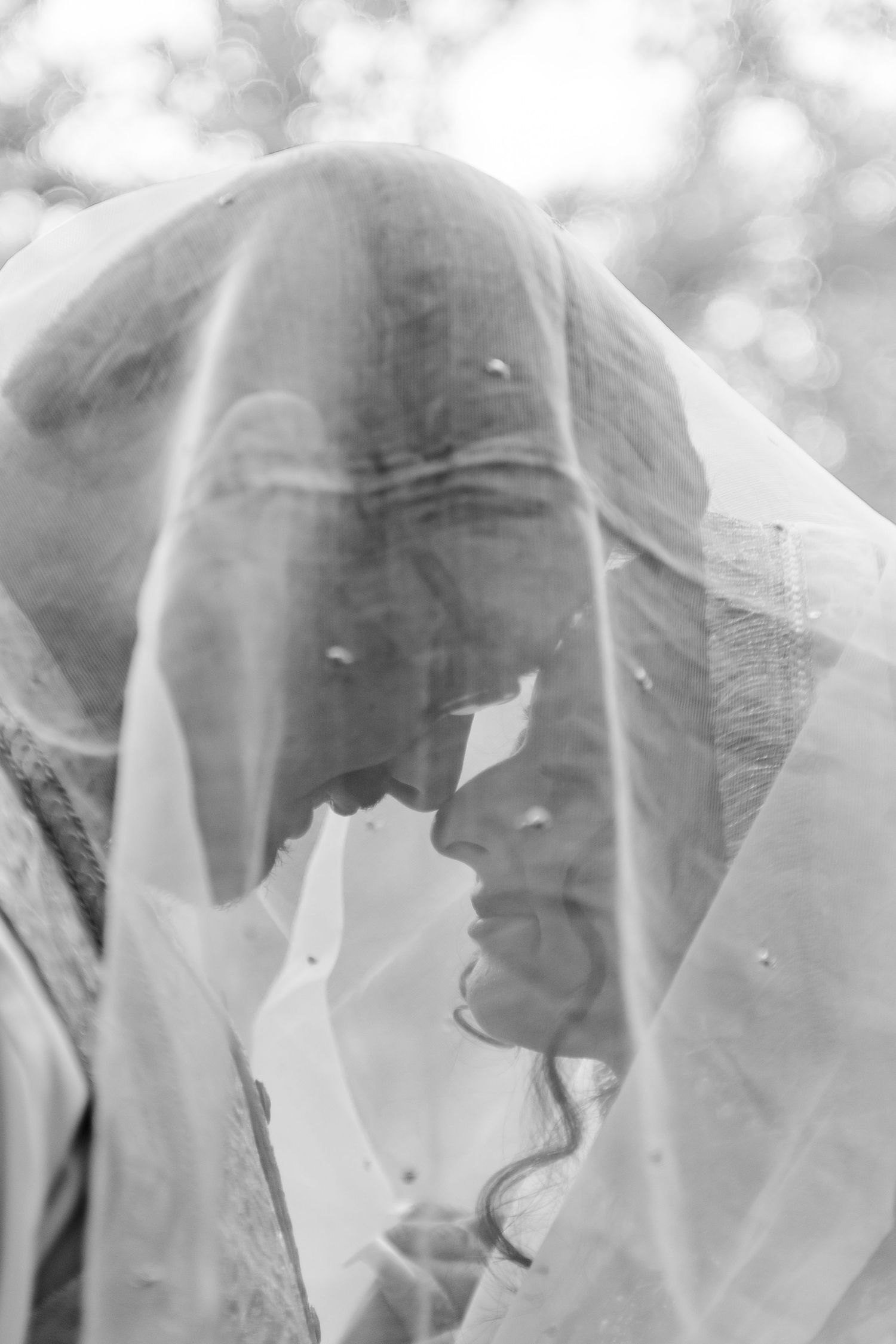 A dreamy black and white portrait through a delicate white veil creating an ethereal romantic effect.