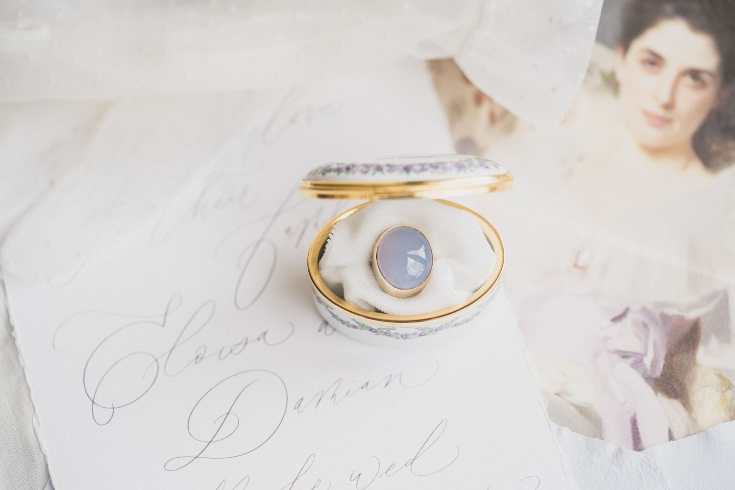 Gold and blue chalcedony ring displayed in a white ceramic box on elegant calligraphy stationery.