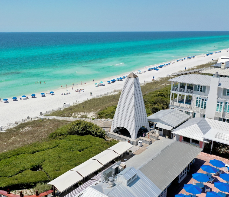 Aerial view of a stunning white sand beach with turquoise water, beach chairs, and coastal buildings in Florida.