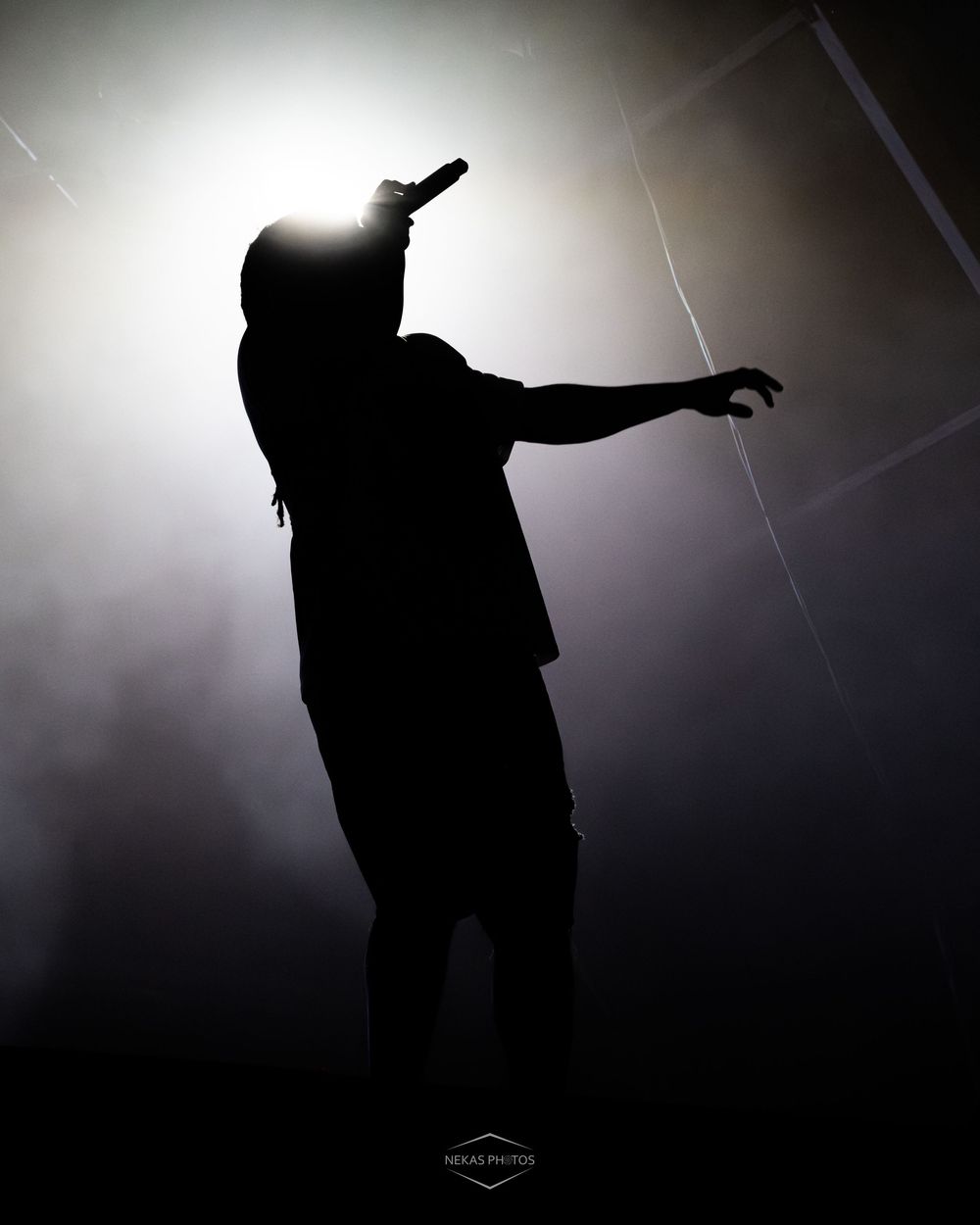 Dramatic silhouette of a performer holding a microphone on stage with bright backlight and smoke effects.
