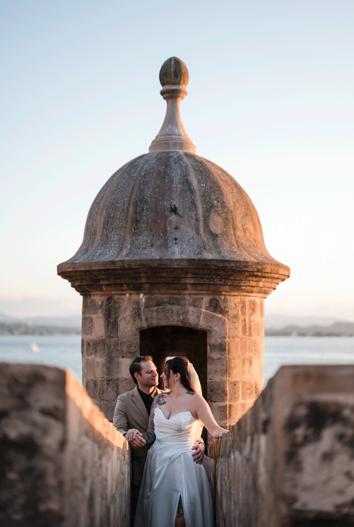 Bride and groom embracing at the top of a historic stone lookout in Old San Juan during golden hour