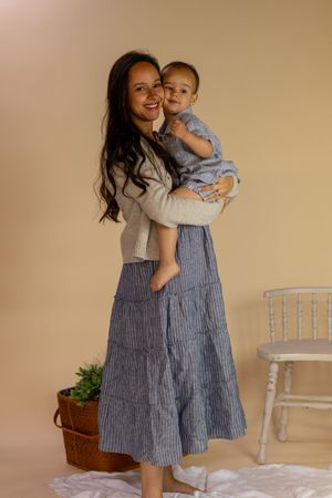 Smiling mother in striped skirt holding happy toddler in blue outfit in beige studio with JBLM photographer in washington state