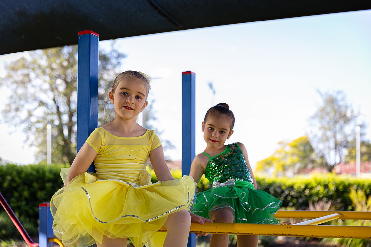 Two girls in dance costumes sitting on a playground during a dance costume photo shoot.