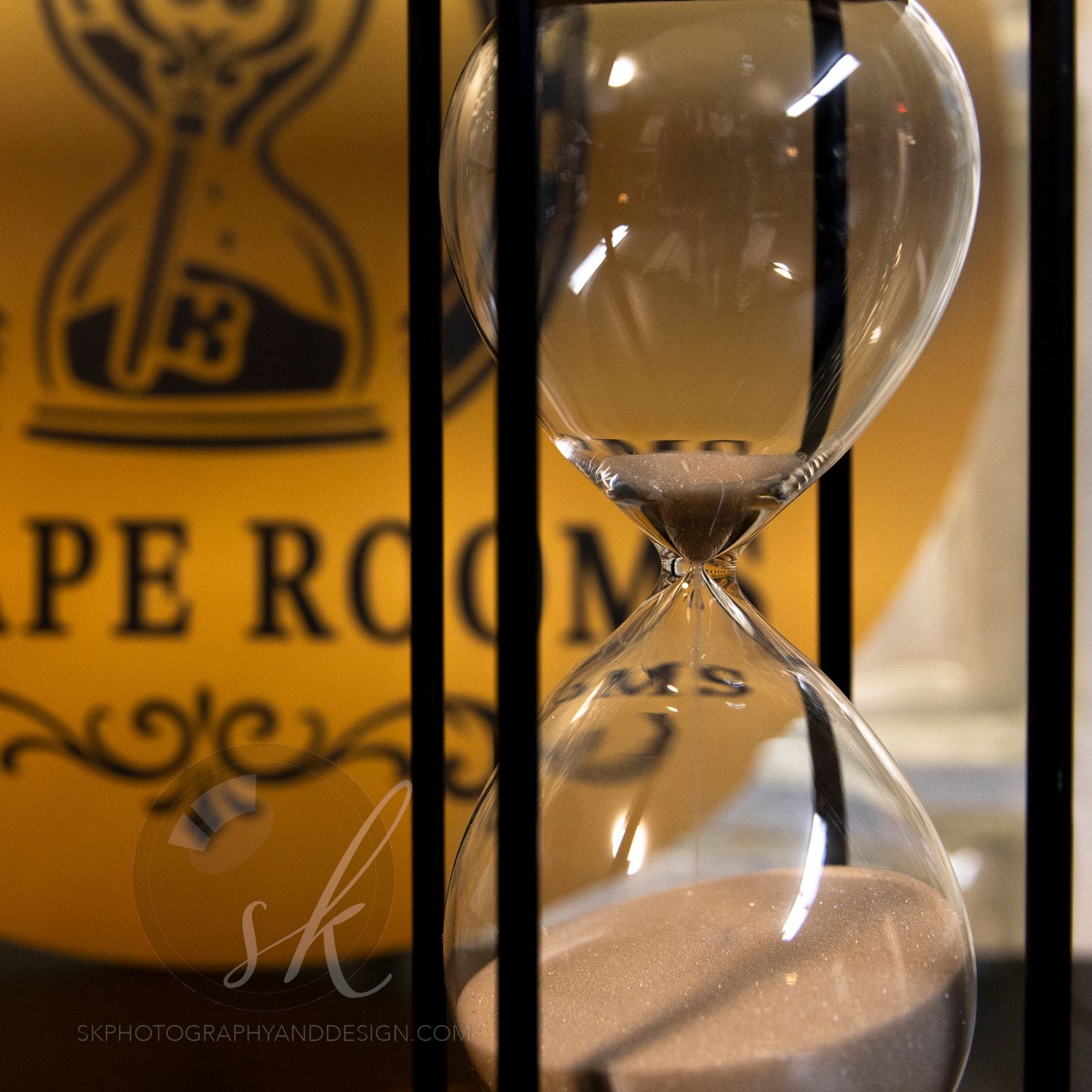 Hourglass with pink sand in front of a yellow Escape Room sign, captured in a dramatic close-up photo.