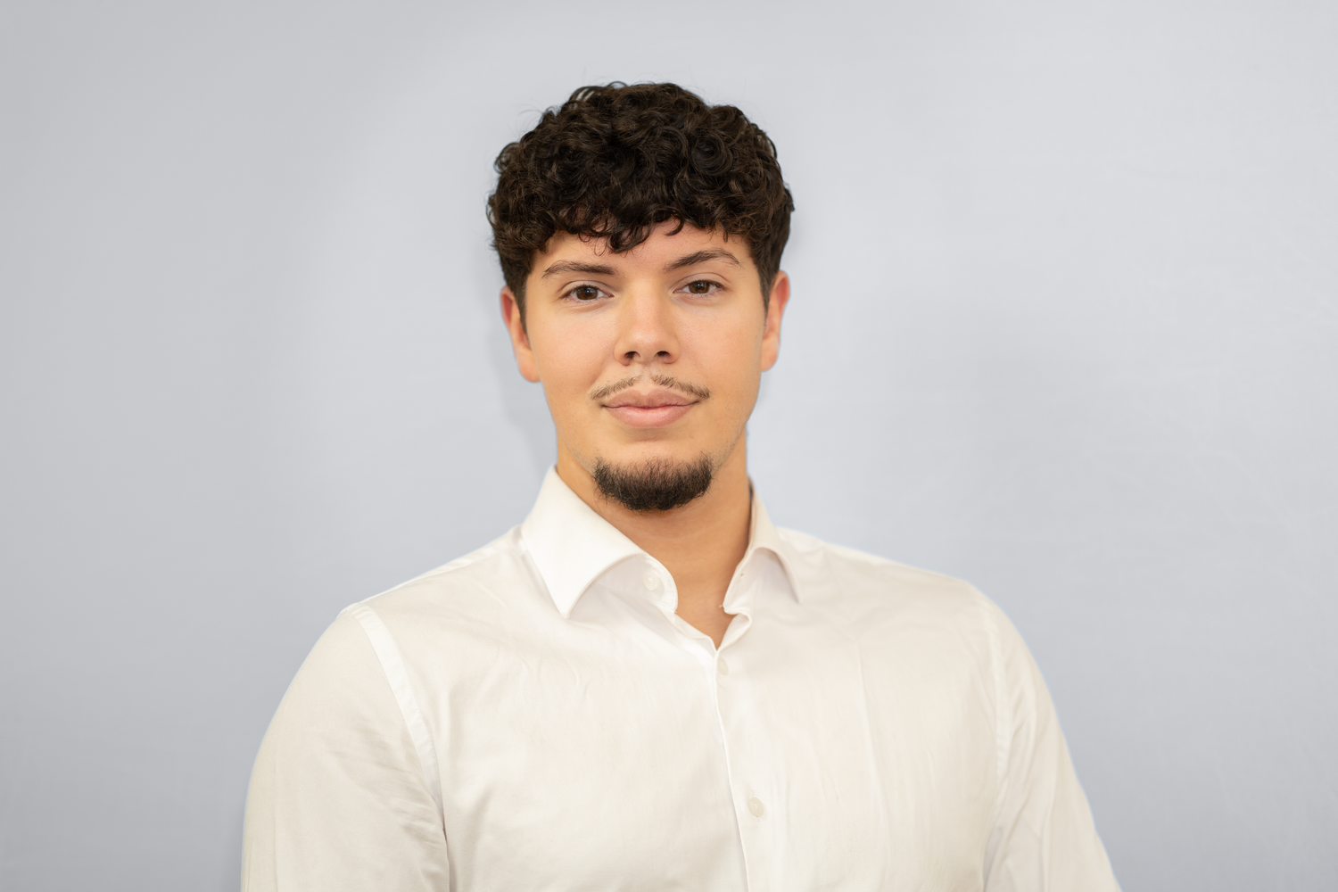 Headshot portrait of young man in white shirt with neutral gray light background.