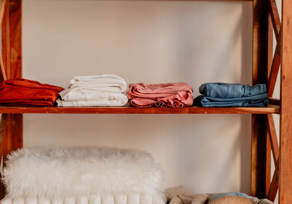Neatly folded colorful towels and linens stacked on rustic wooden shelves with a fluffy white blanket below.