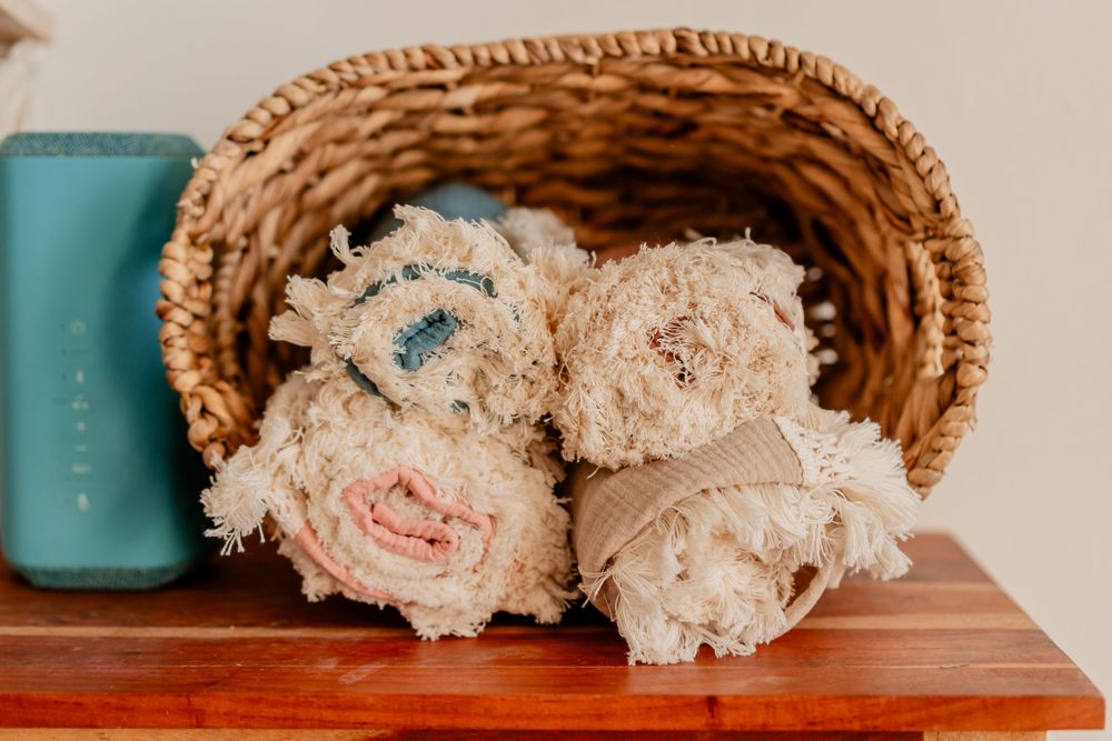 Wicker basket filled with rolled vintage distressed cotton rugs on a wooden shelf.