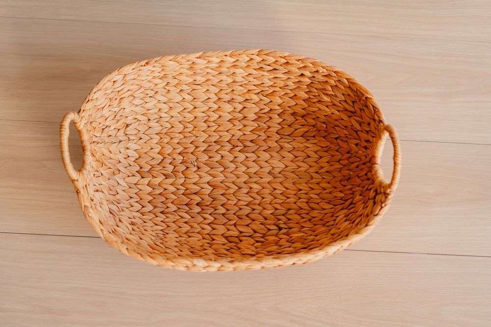 Empty oval woven seagrass basket with handles, viewed from above on a light wood surface.