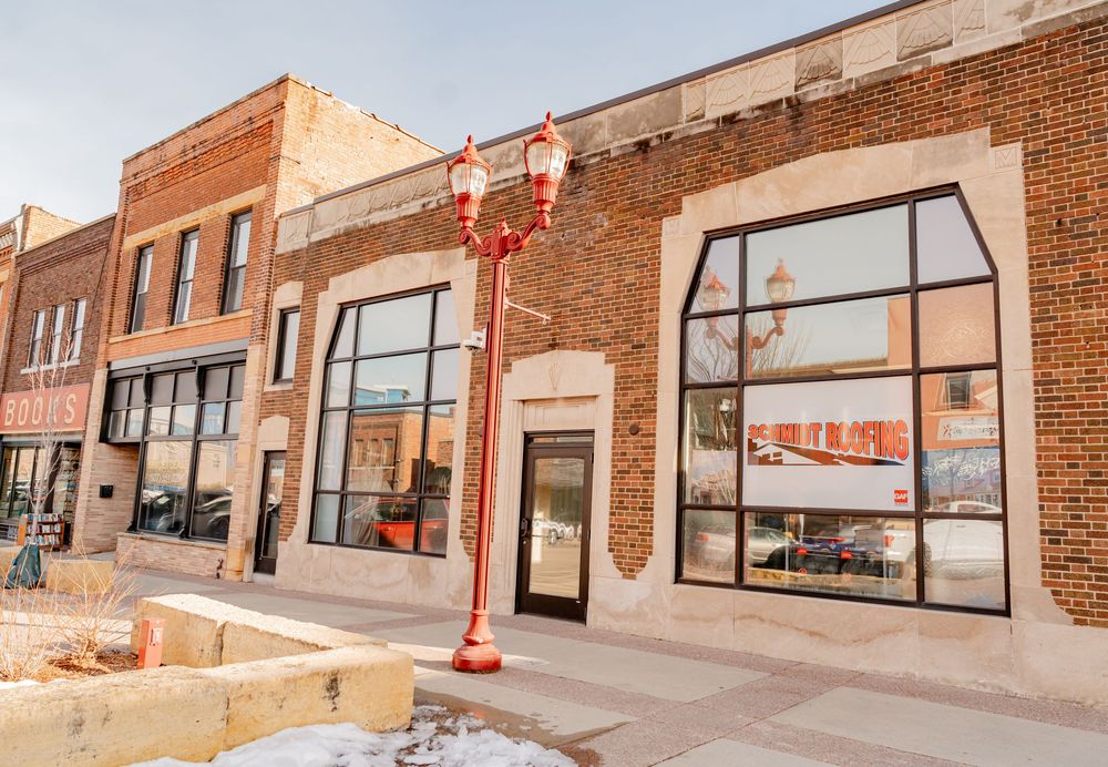 Historic brick storefront with large arched windows, red lamp post, and snow-dusted sidewalk in a small town downtown district.