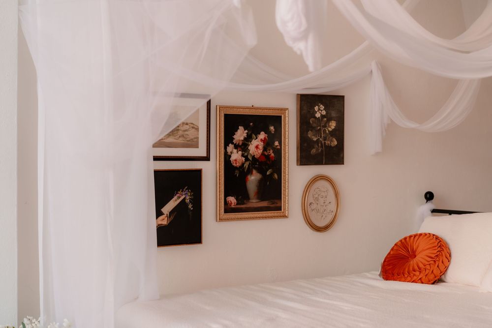 White canopy bed with gallery wall featuring floral and botanical art prints in a bright minimalist bedroom.