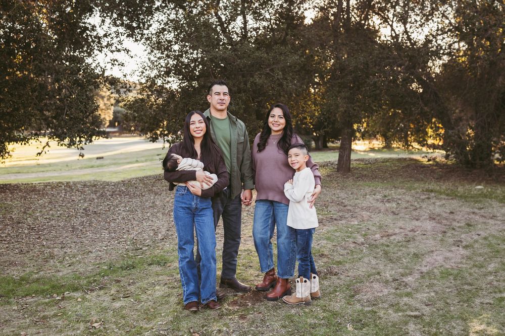 Family of four posing outdoors in a park with tall trees, wearing casual fall outfits including jeans and sweaters.