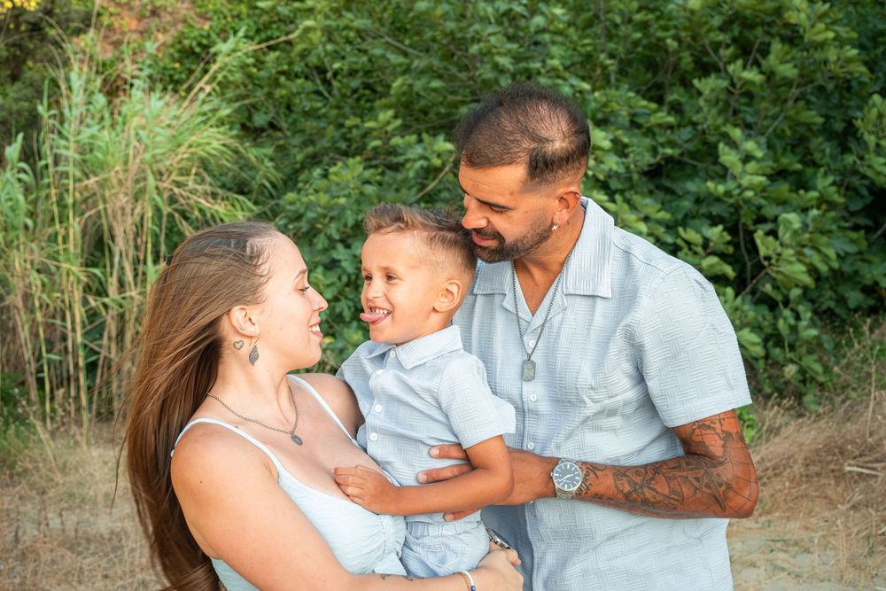 Happy family of three smiling outdoors, parents holding young toddler boy in nature setting.