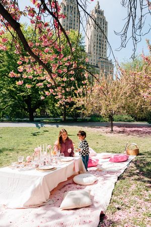 Mother and child enjoying a elegant picnic table setup under pink cherry blossoms in Central Park, NYC.