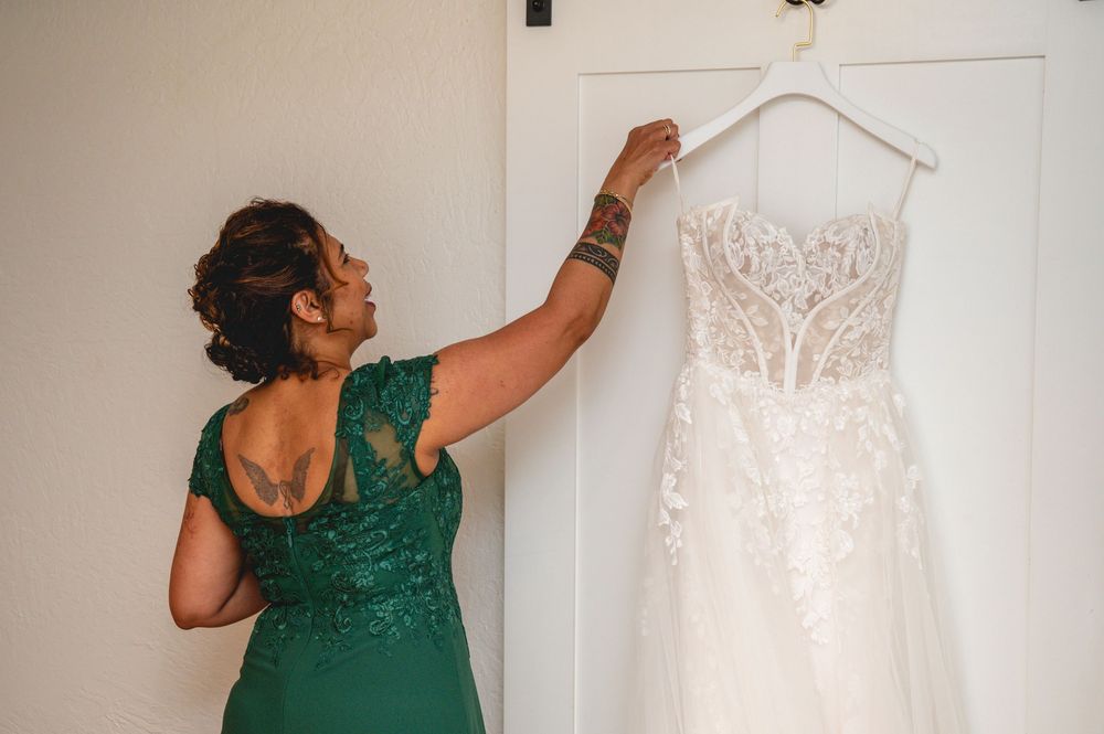 Woman in green dress admiring a white lace wedding gown hanging on a door before the ceremony.