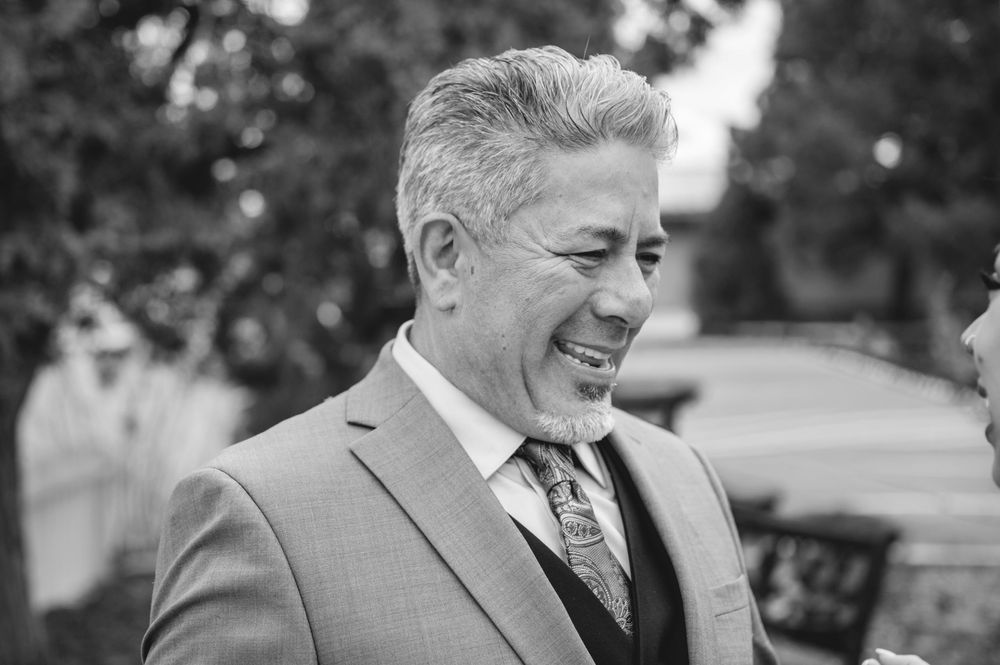 Smiling middle-aged man in a suit and patterned tie at an outdoor event, black and white photo.