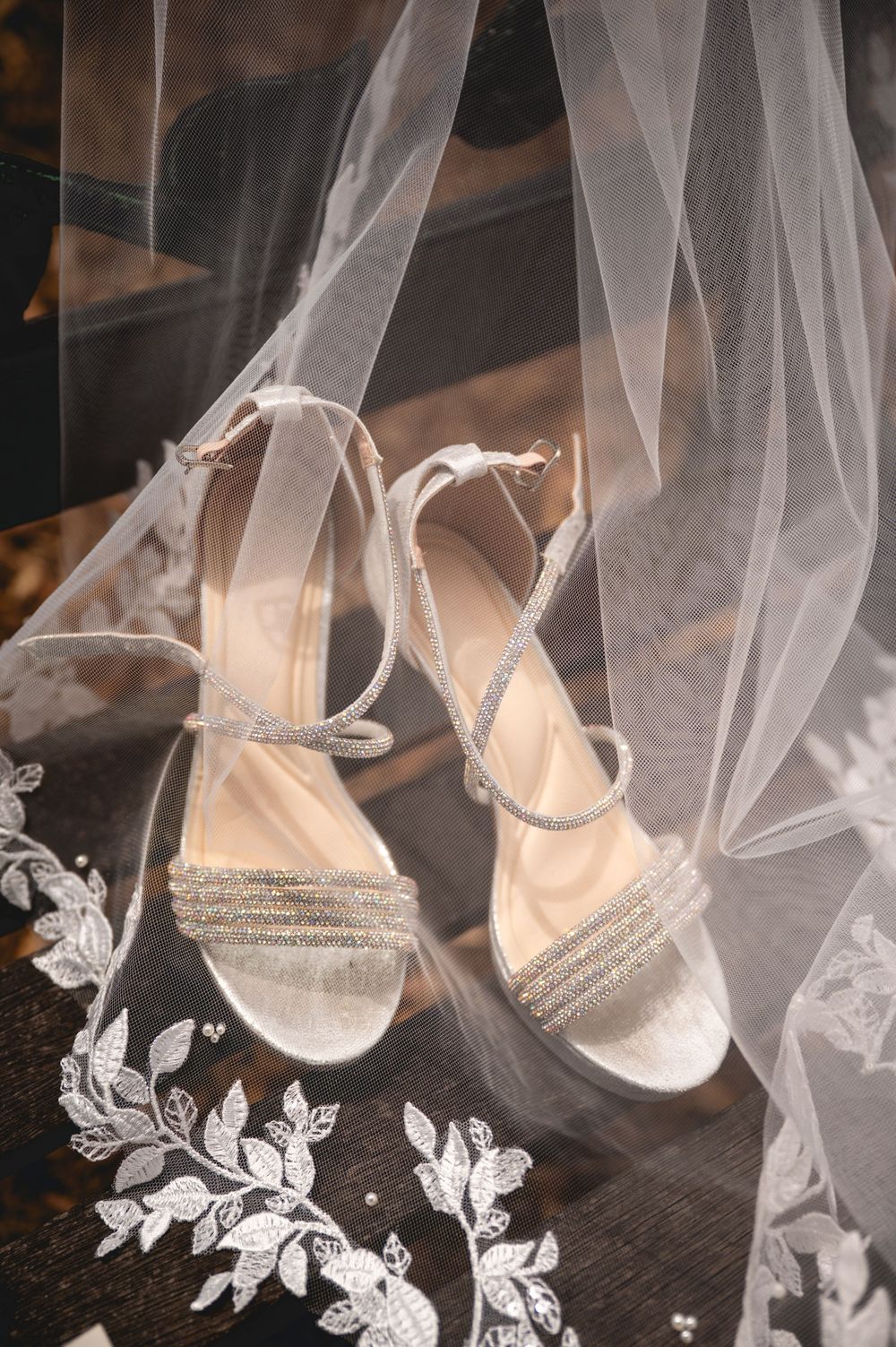 Elegant silver glitter block heel wedding sandals with ankle straps displayed on lace fabric beneath a sheer bridal veil.
