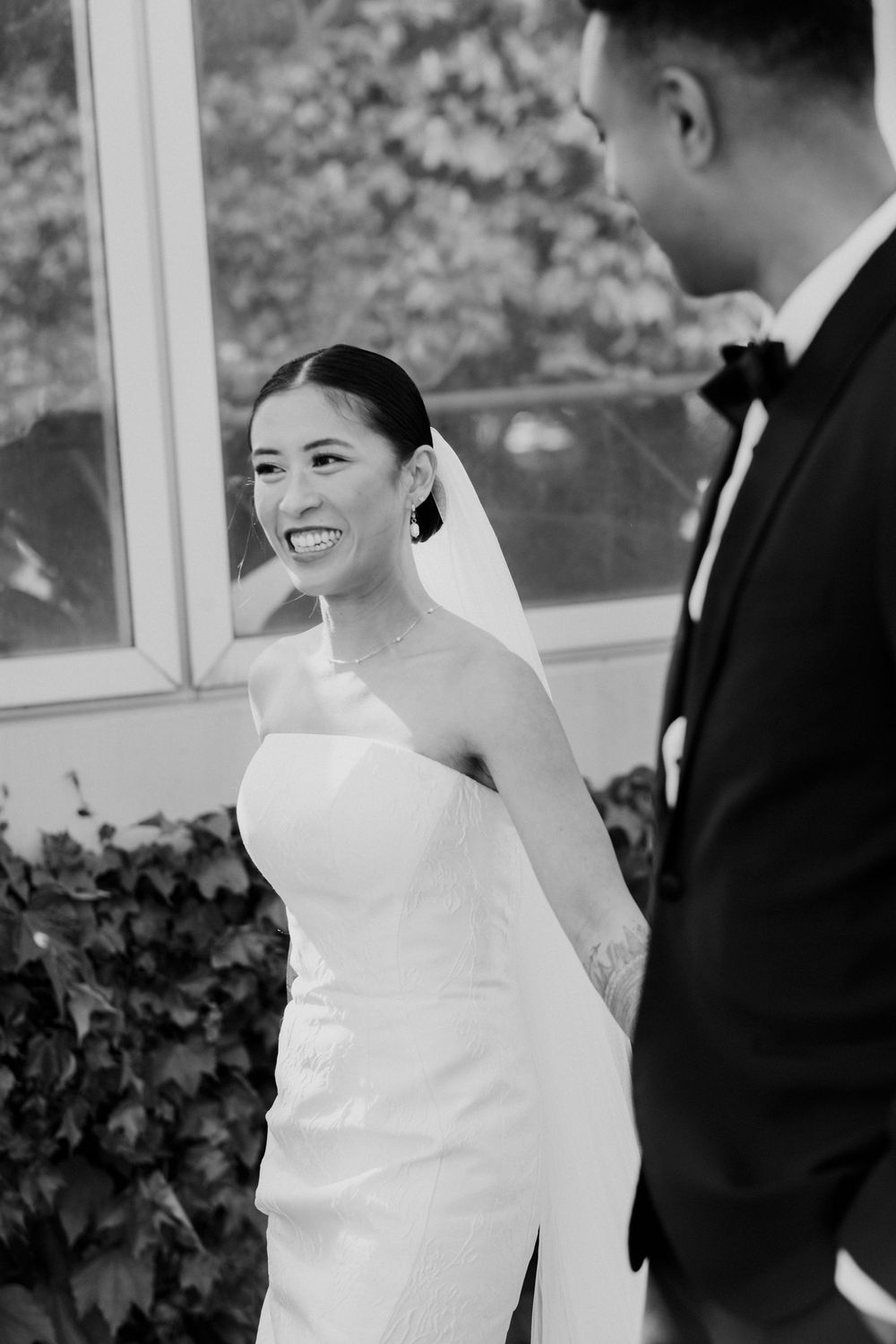 Candid photo of radiant bride in strapless white wedding gown smiles joyfully at groom during Chicago wedding day in black and white photo.