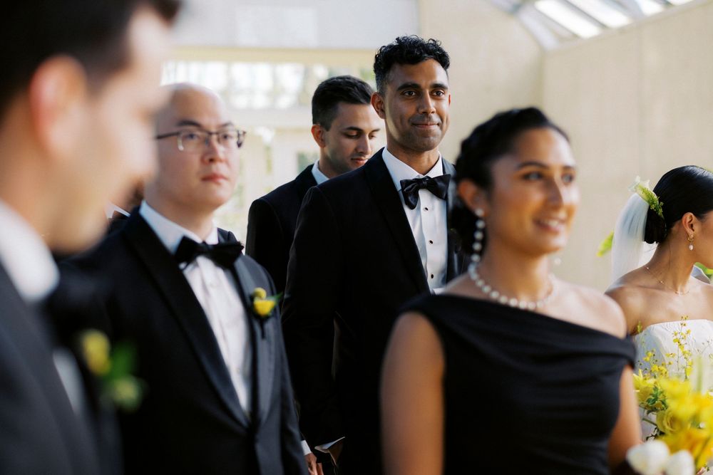 Wedding party in formal attire, groomsmen in tuxedos with bow ties and bridesmaids in black dresses with pearls.