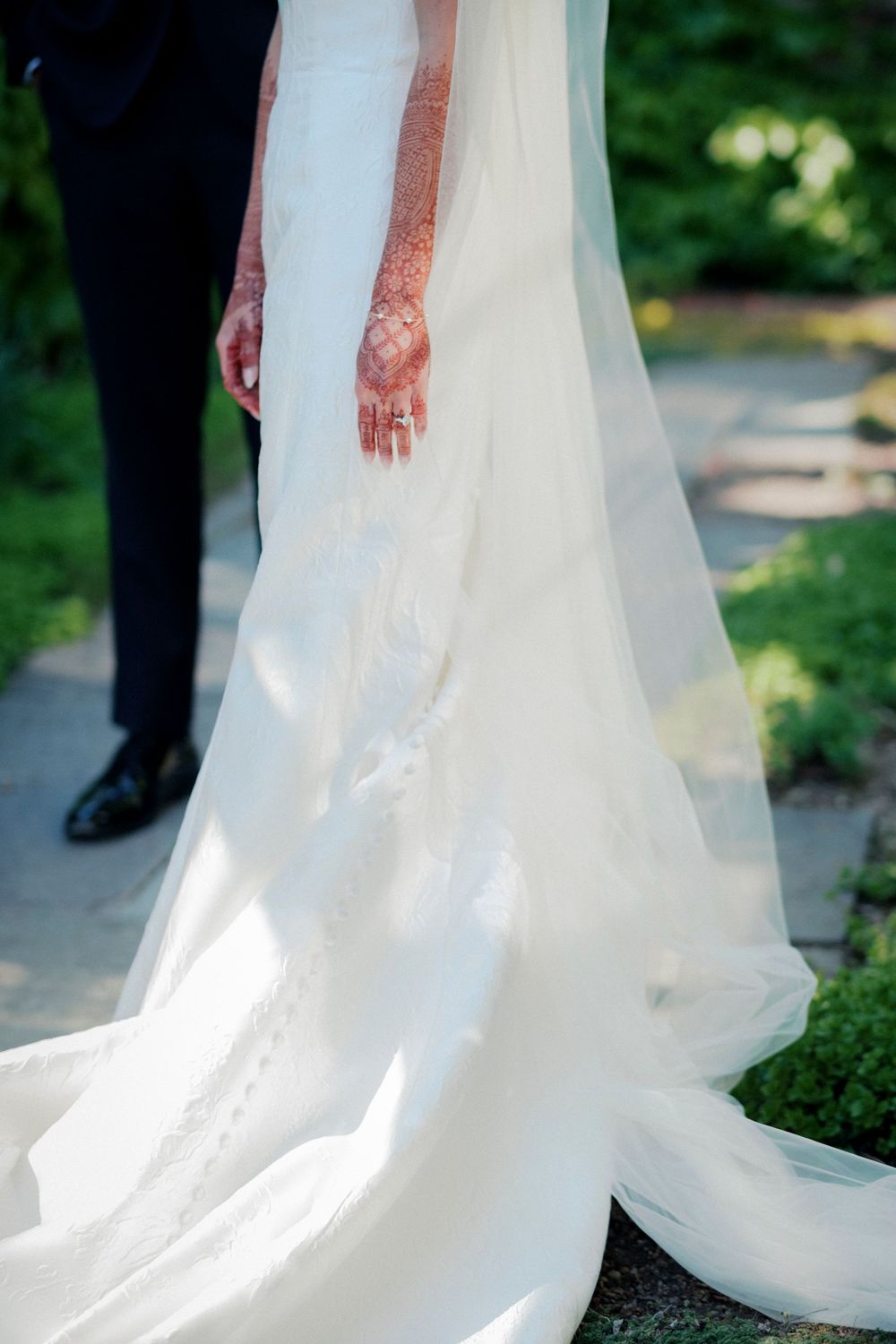 Close-up of bride in white wedding gown with lace train and henna-adorned hands outside Garfield Park Conservatory wedding.