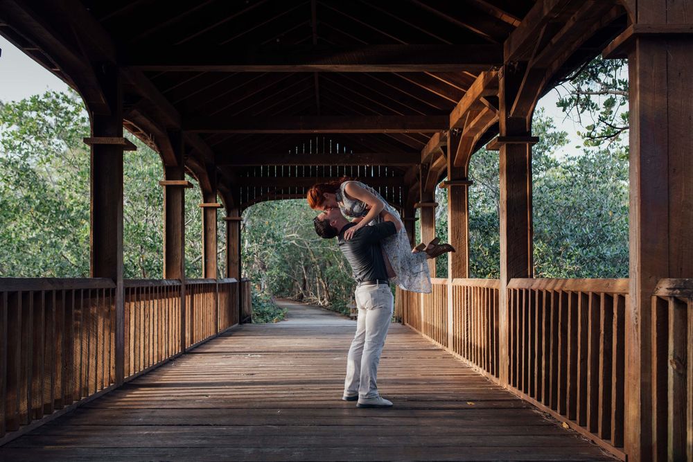Couple sharing a romantic dip on a wooden covered bridge surrounded by lush green trees.
