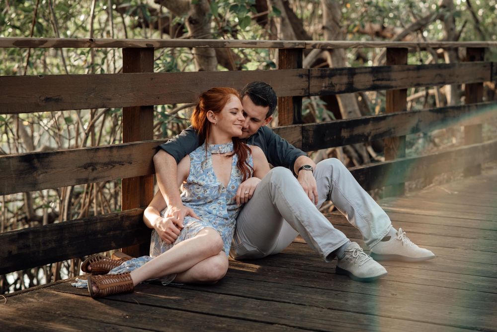 Couple sitting closely together on a wooden bridge deck, sharing a tender moment outdoors.