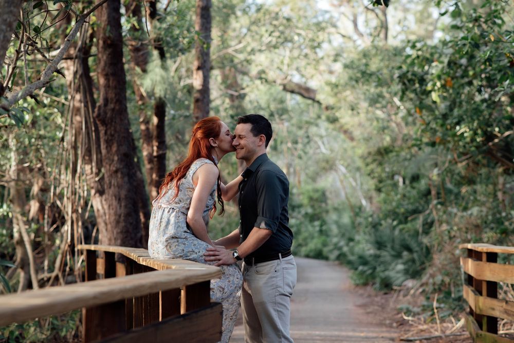 Romantic couple sharing a close moment on a wooden bridge surrounded by lush forest trees.