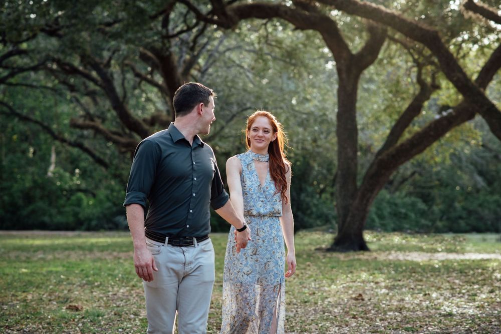 Couple walking together in a lush green park, woman in floral dress and man in dark shirt, sharing a joyful moment.