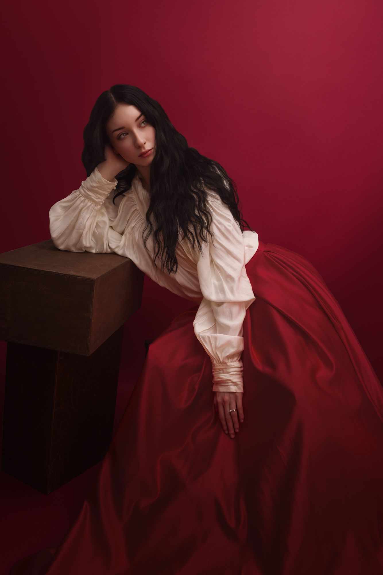 Woman in white ruffled blouse and red ball gown skirt poses against red background in vintage-inspired fashion portrait.