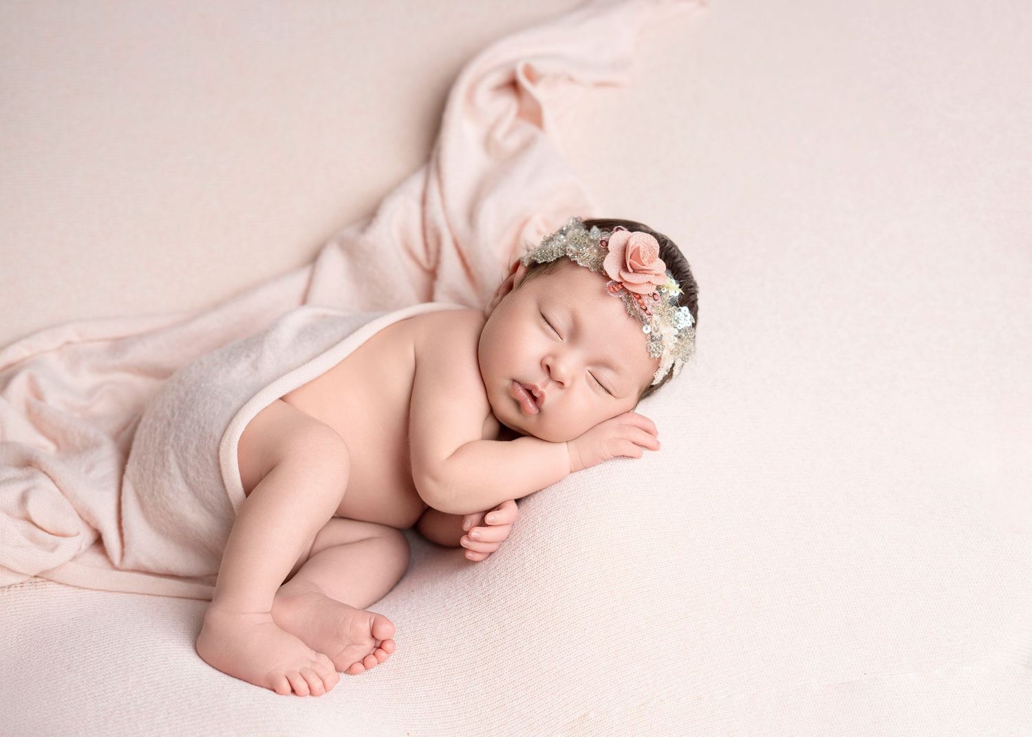 Newborn photography Covina CA sleeping baby girl with floral headband on soft neutral studio backdrop.