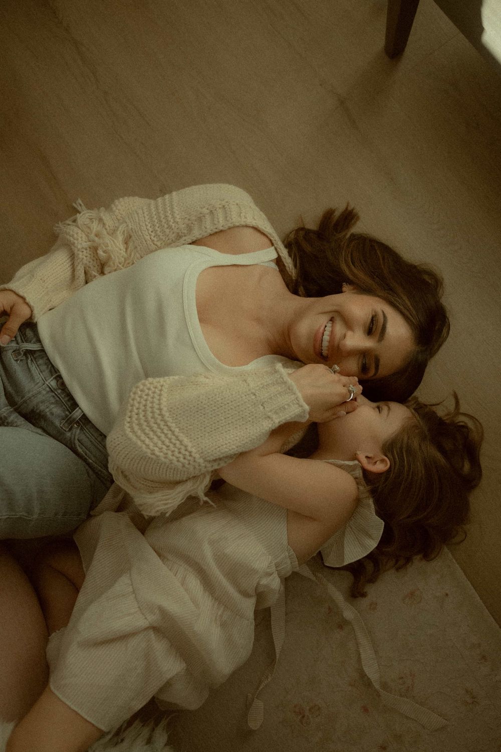 Mother and daughter laughing together while lying on floor, sharing a joyful moment.